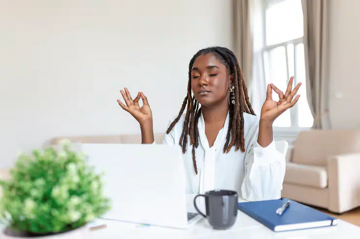 Femme en méditation devant son ordinateur de travail afin de pouvoir travailler avec un esprit tranquille.